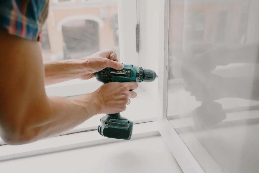service request - person fixing white window frame with a drill
