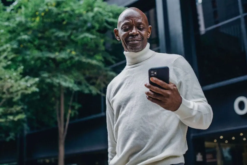 man outside building holding a phone and looking at text messages from his condo association