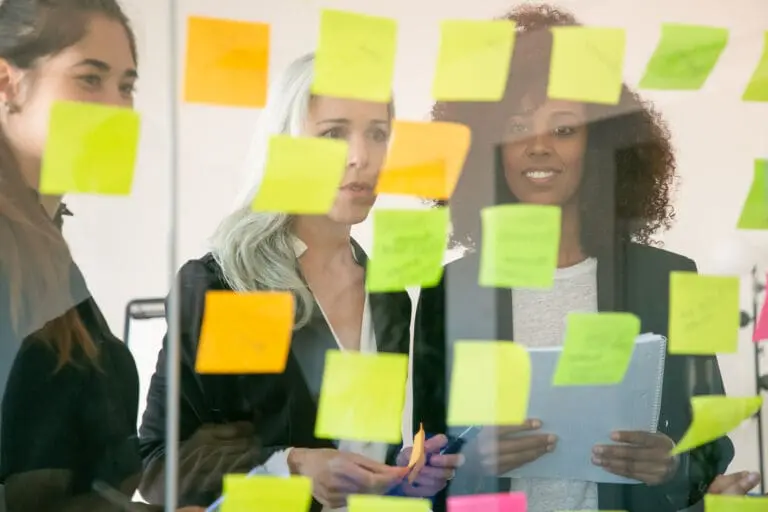 Three women engaged in a discussion, using post-it notes to figure out how to run an HOA
