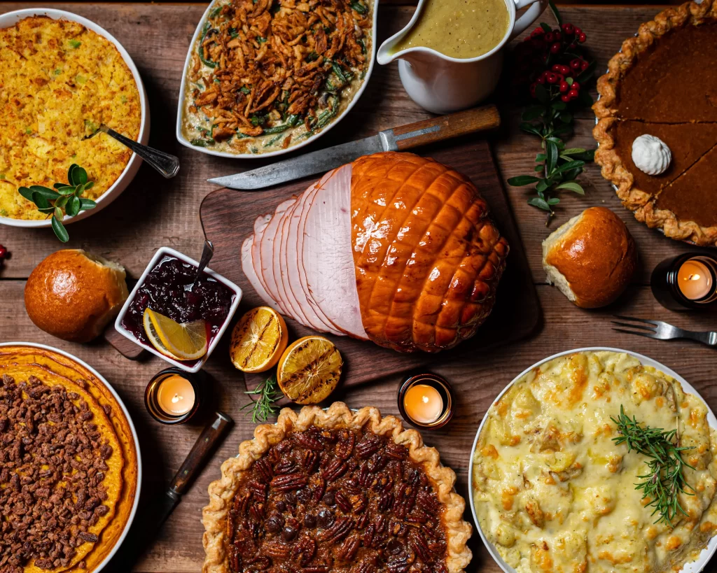 image of different thanksgiving dishes: ham, 4 pies, pumpkin and other food