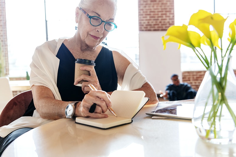 Older woman holding a coffee writing in a notebook - condo association newsletter