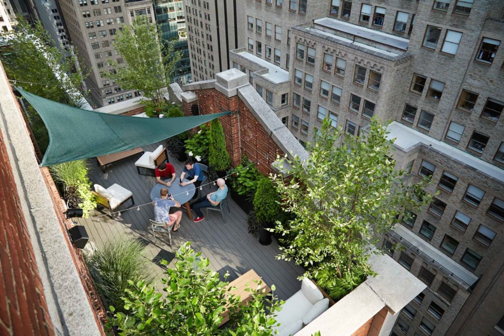 an example of condo landscaping - a city rooftop with plants, a table, chairs and people talking