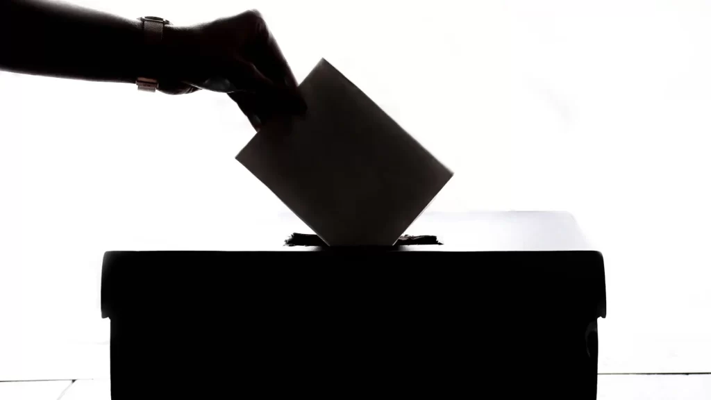 white background with a black voting box and a hand putting an envelope in it to represent HOA voting fraud