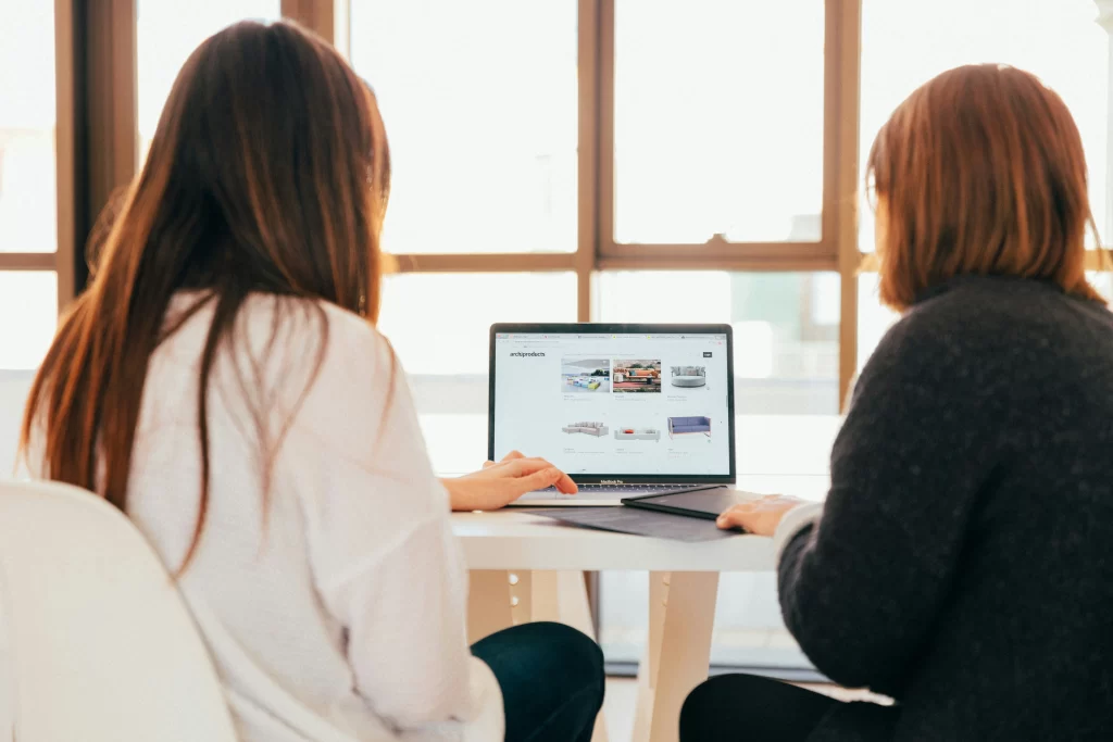 Two women seated, facing a computer screen, engrossed in learning about the new Florida HOA Website Law