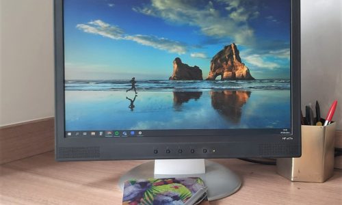 Image of computer screen with notebook and pen in the front and a gold pot of pens to the right