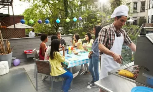 A man in an apron grills while 5 people site around a table talking in their outdoor amenities
