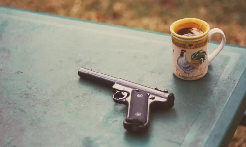 gun on a table with a mug. HOA guns