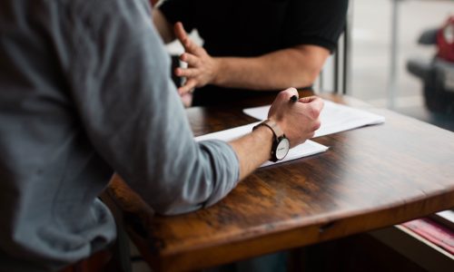 Two individuals seated at a table during a meeting, one person diligently writing down HOA meeting minutes