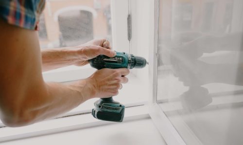service request - person fixing white window frame with a drill